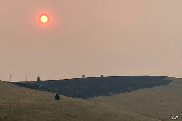 Smoke obscures the air and dims the sun over a hillside burned by a recent wildfire, in Missoula, Mont., on Sunday, July 18,…