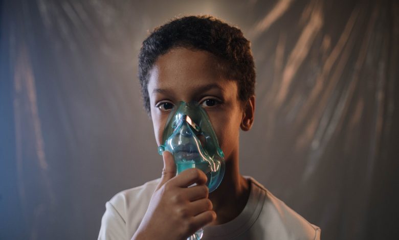 a boy in white shirt holding green oxygen mask