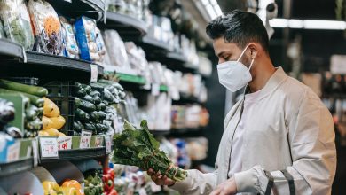 young ethnic guy buying bunch of fresh spinach in supermarket