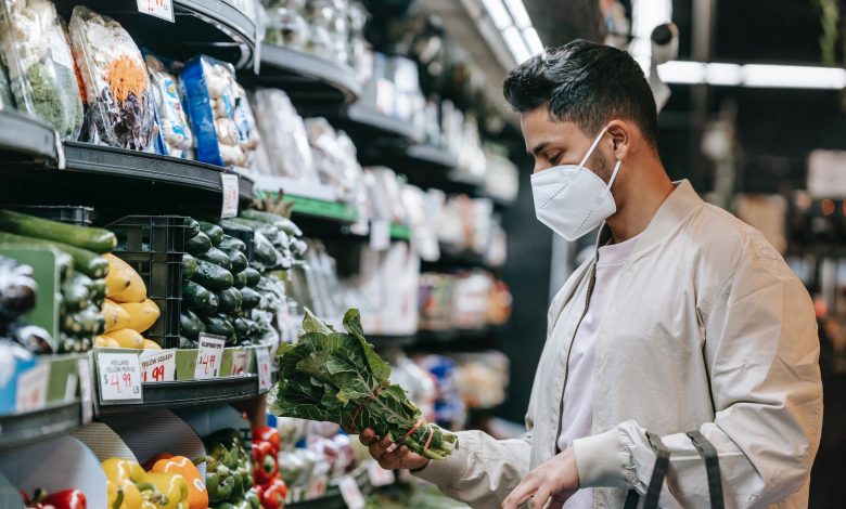 young ethnic guy buying bunch of fresh spinach in supermarket