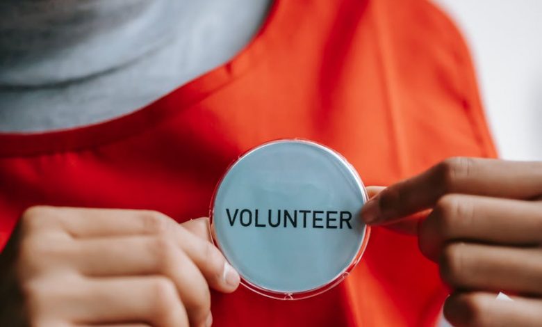 smiling ethnic woman showing volunteer sign on red apron